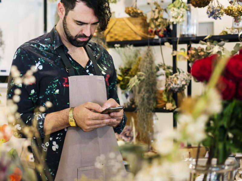Bearded man using mobile phone in flower shop
